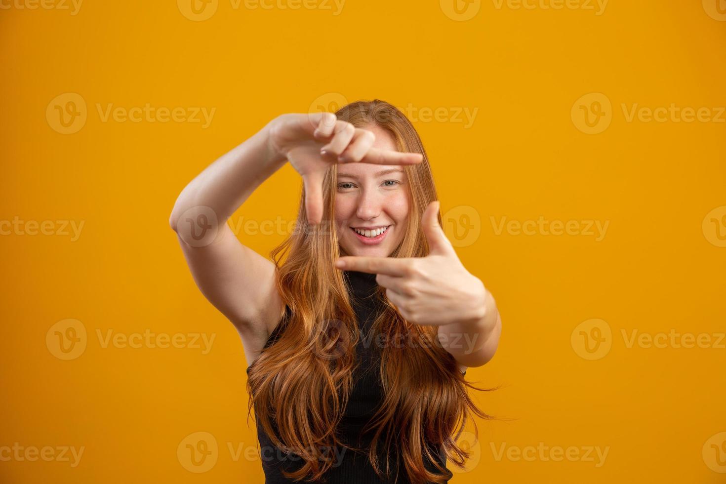 Redhead caucasian woman over yellow isolated background smiling making frame with hands and fingers with happy face. Creativity and photography concept. Film-maker or photographer. Lens vision idea. photo
