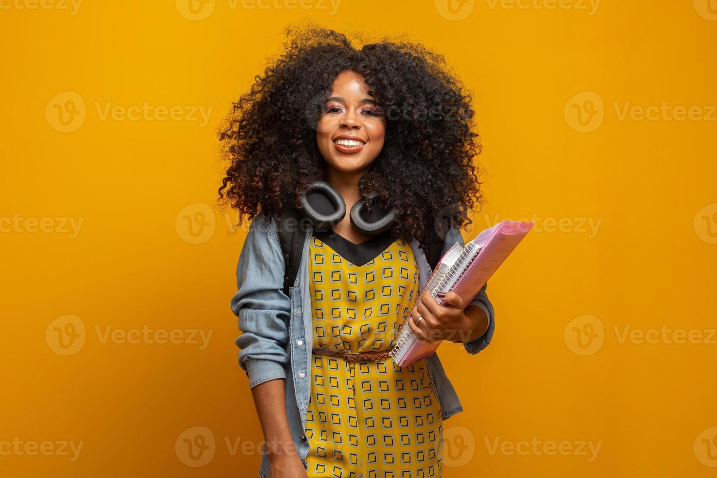 Female student in campus with books in her arms. Yellow background. photo