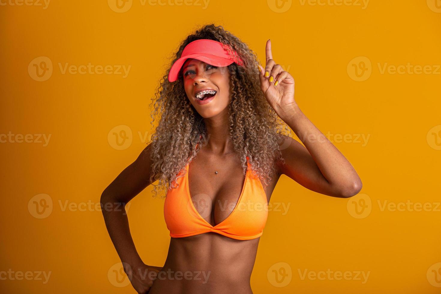 Attractive curly hair girl in a orange bikini, hat, emotionally opened mouth on a yellow background with a perfect body. Isolated. Studio shot. photo