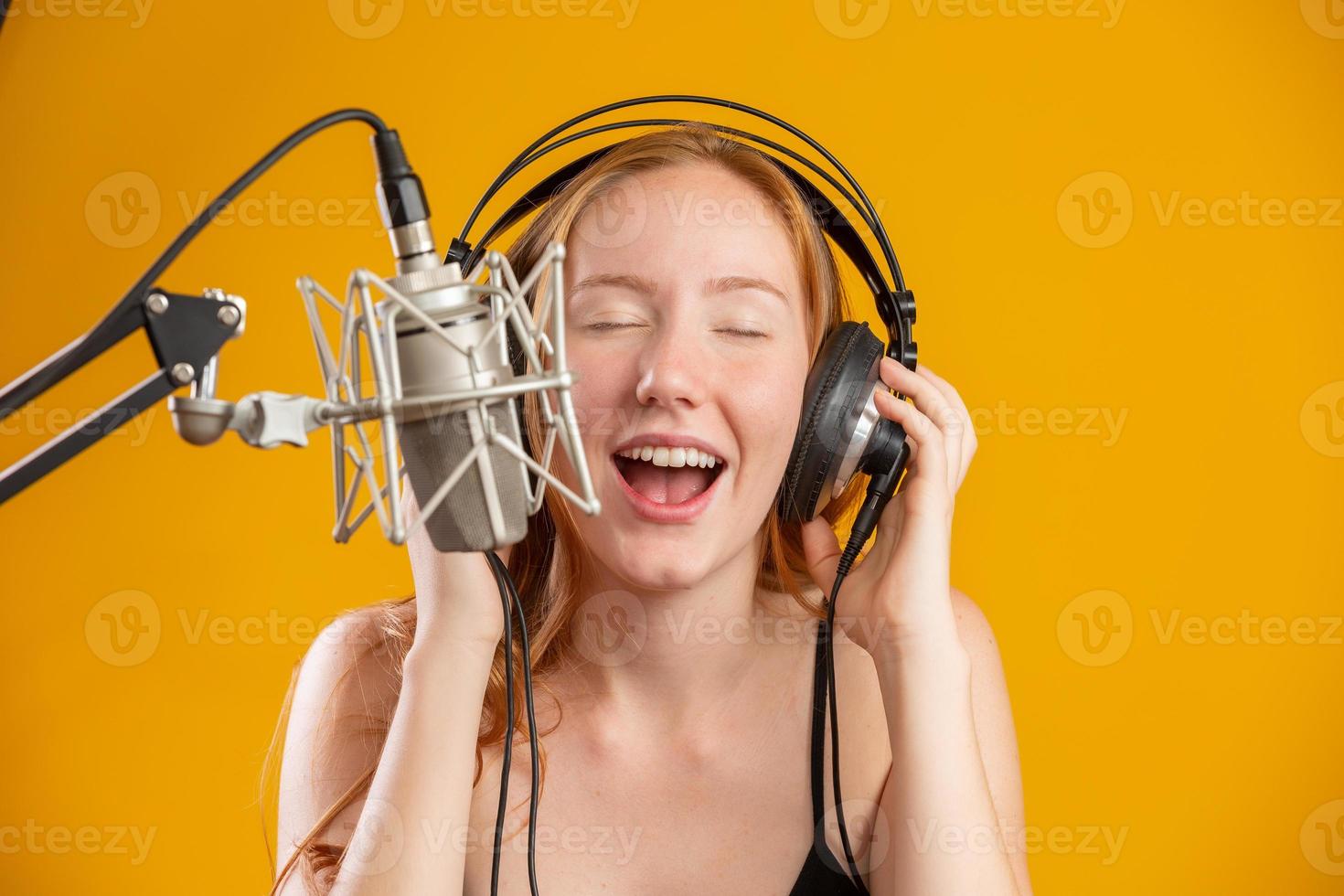 hermosa pelirroja cara de mujer cantando con un micrófono condensador de plata con la boca abierta interpretando una pose de canción sobre un espacio de copia de fondo amarillo para su texto. locutor de radio fm. foto