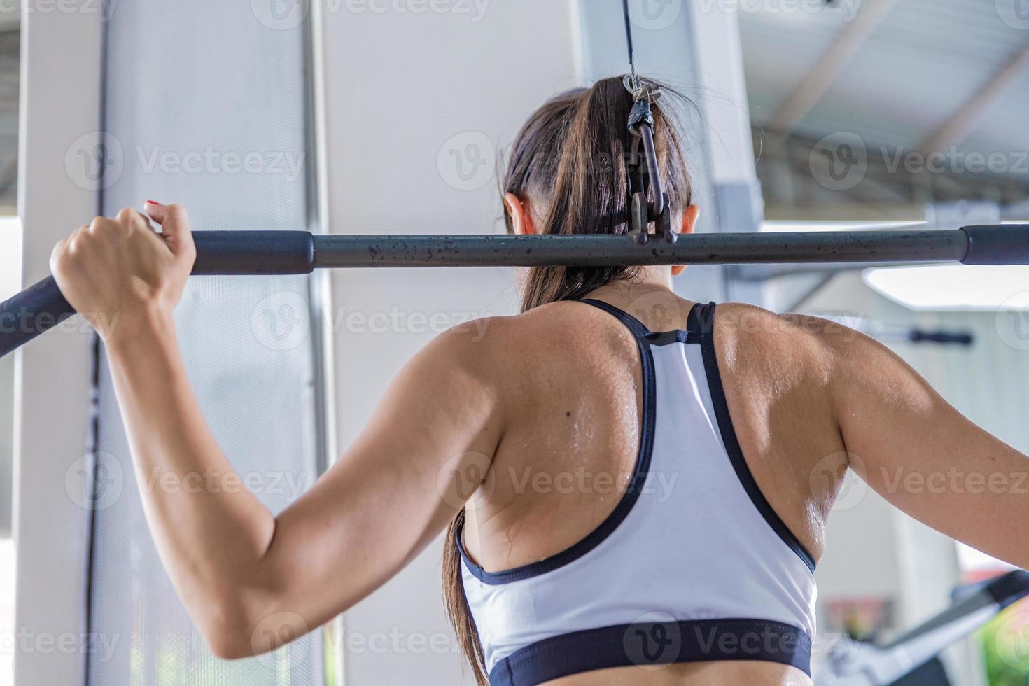 Athletic woman using machine for pumping back muscles in gym, back view photo