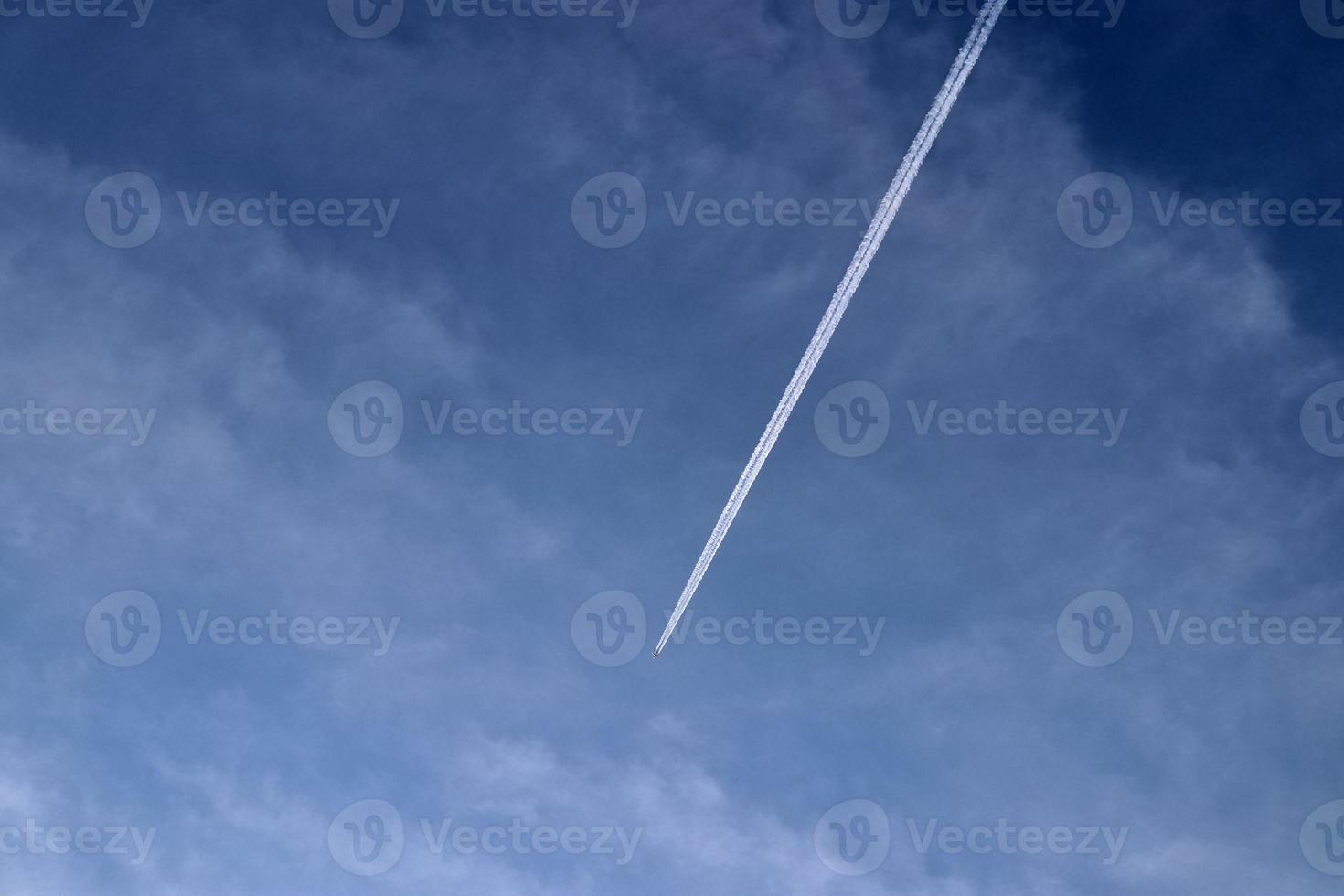 Aircraft condensation contrails in the blue sky inbetween some clouds photo