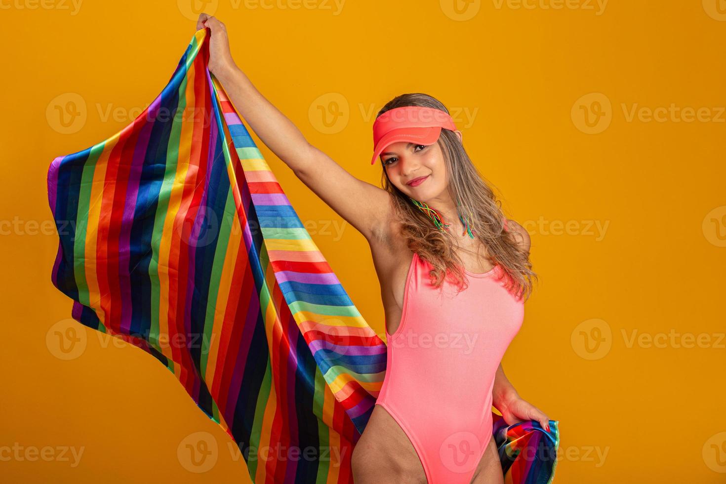 Young blonde hair woman covering with lgbt pride flag. Alone. One. Keeping fist up, covering LGBT flag. LGBT flag on yellow background. photo