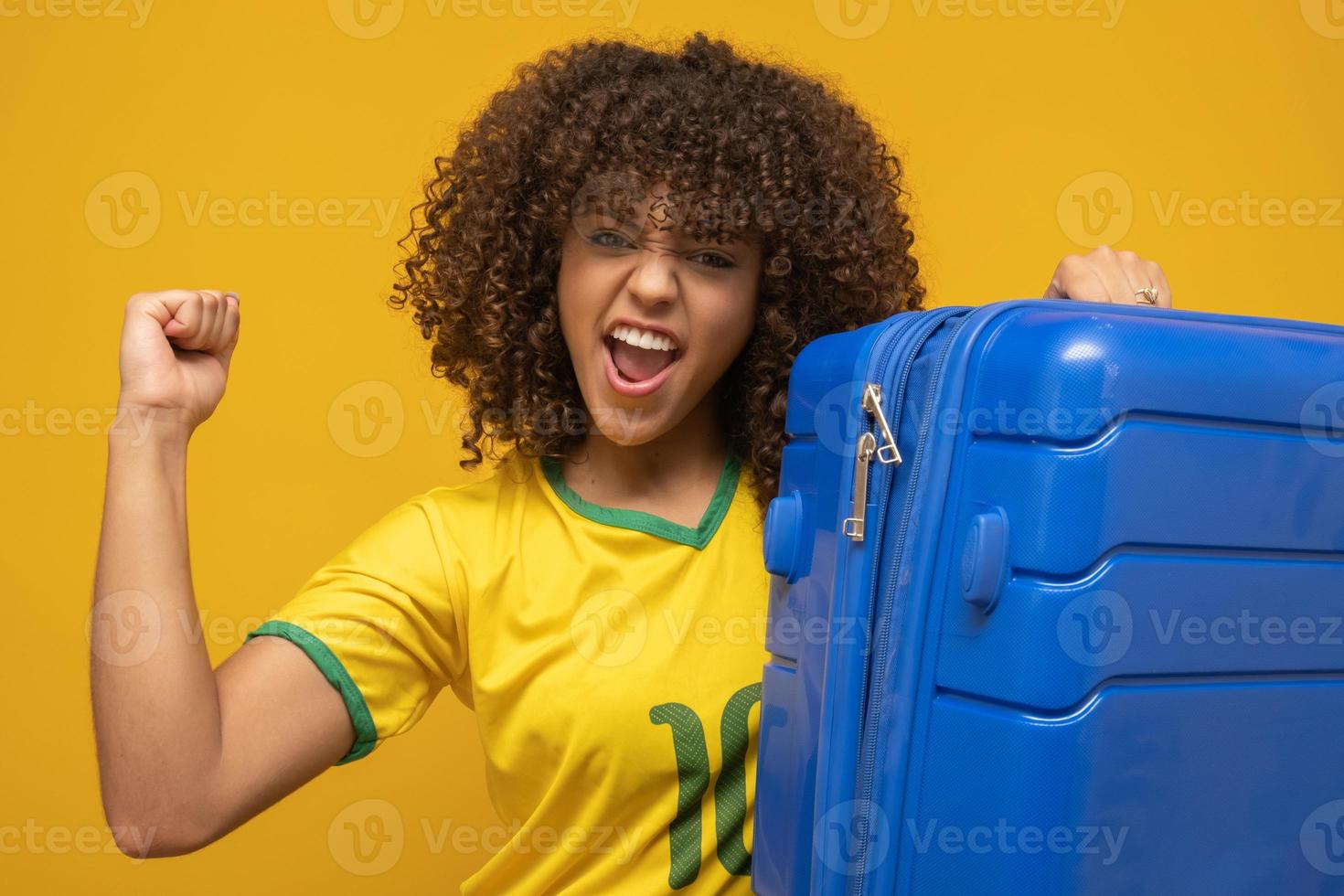 Funny woman holding a heavy travel bag. On yellow background. Brazilian player with bags ready to see Brazil play in the World Cup photo