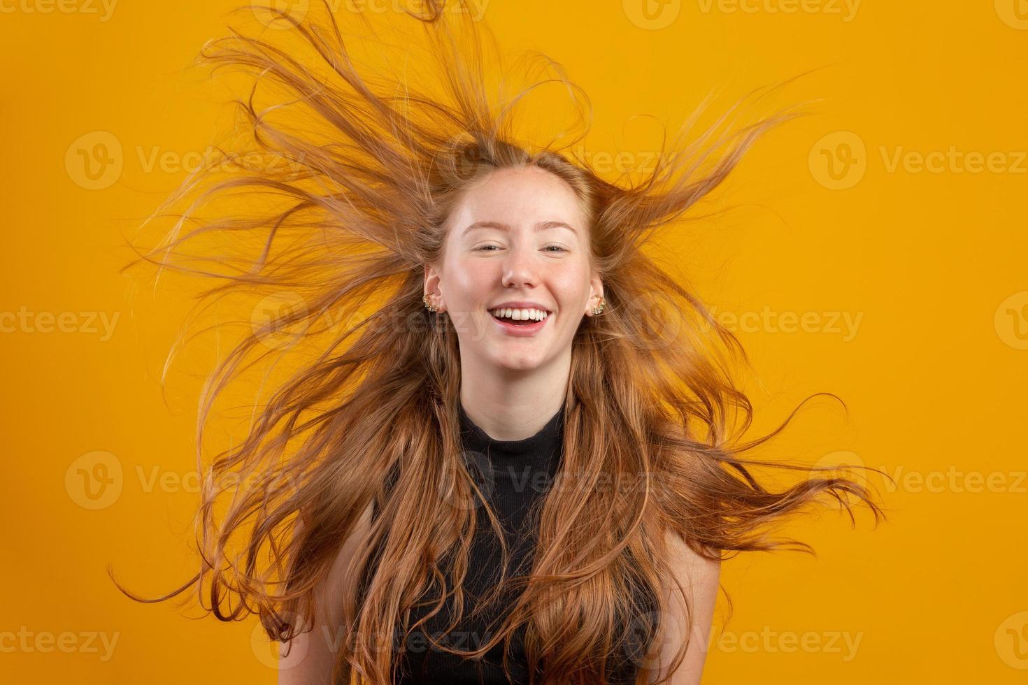 Portrait of beautiful cheerful redhead girl with flying hair smiling laughing looking at camera over yellow background. photo