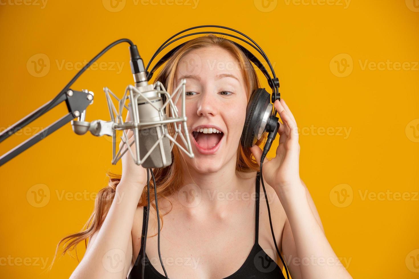 hermosa pelirroja cara de mujer cantando con un micrófono condensador de plata con la boca abierta interpretando una pose de canción sobre un espacio de copia de fondo amarillo para su texto. locutor de radio fm. foto