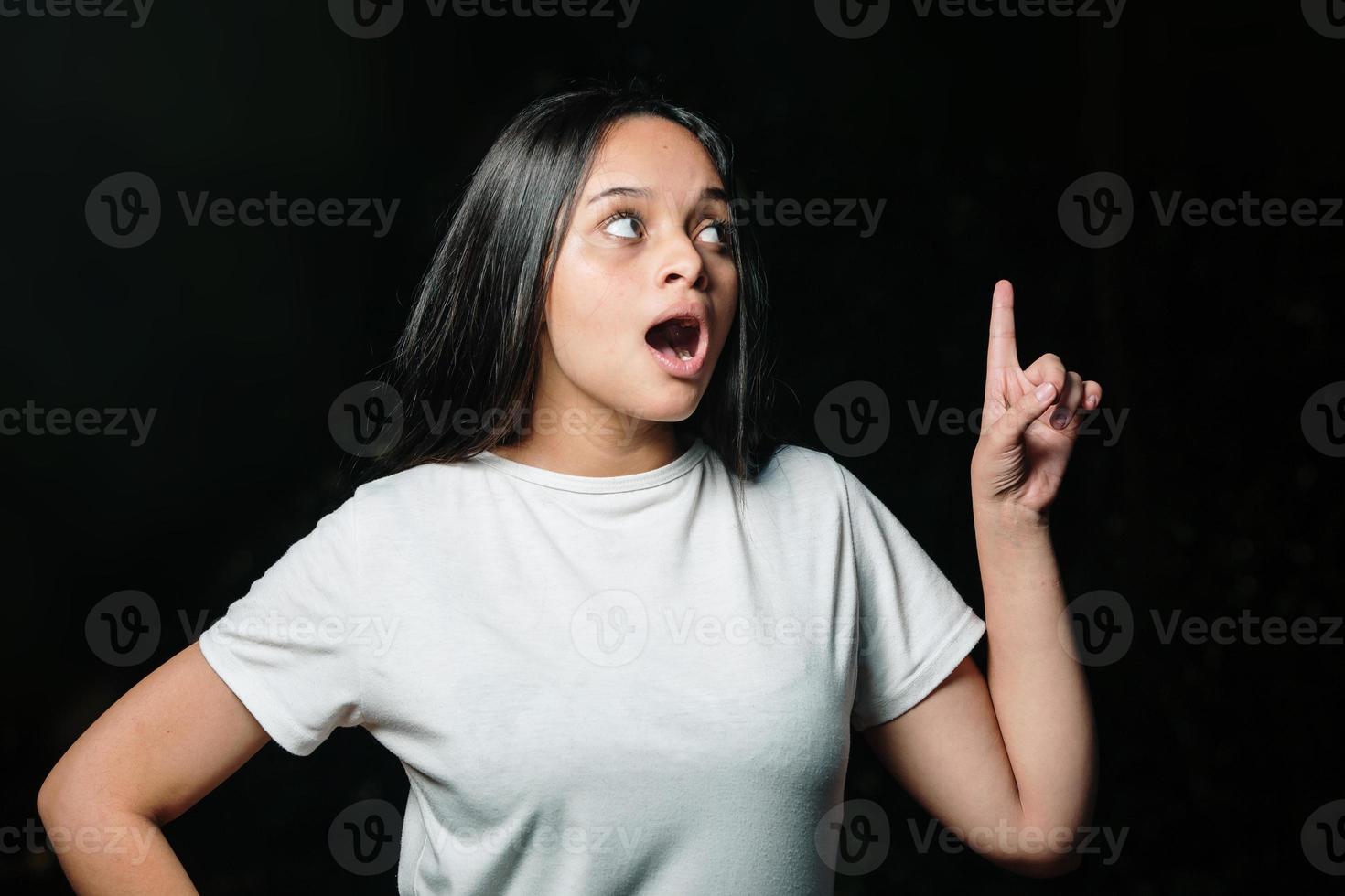 retrato de una adolescente señalando una gran idea, en un fondo oscuro. idea increíble. hermosa joven adolescente manteniendo el dedo hacia arriba. niño lindo feliz tiene una idea inesperada. foto