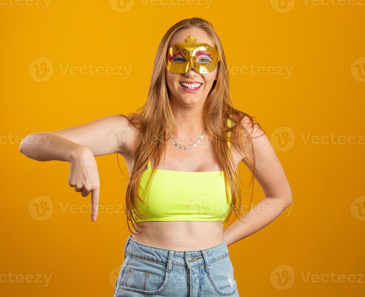 Beautiful woman dressed for carnival night. Smiling woman ready to enjoy the carnival with a colorful mask. Pointing down. photo