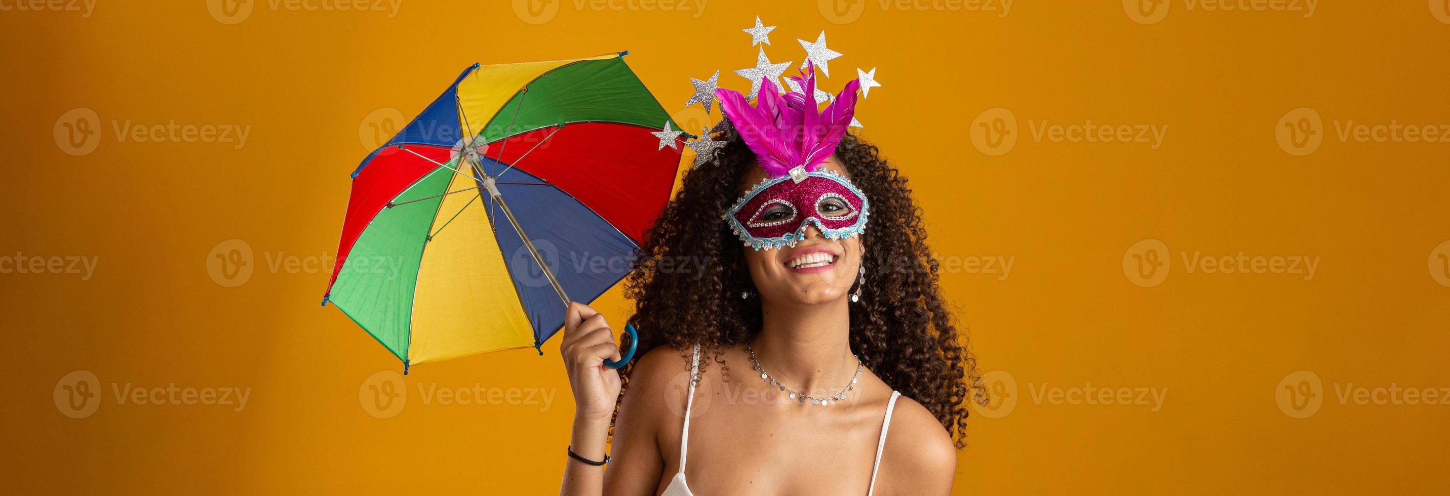 mujer joven de pelo rizado celebrando la fiesta del carnaval brasileño con paraguas frevo en amarillo. foto