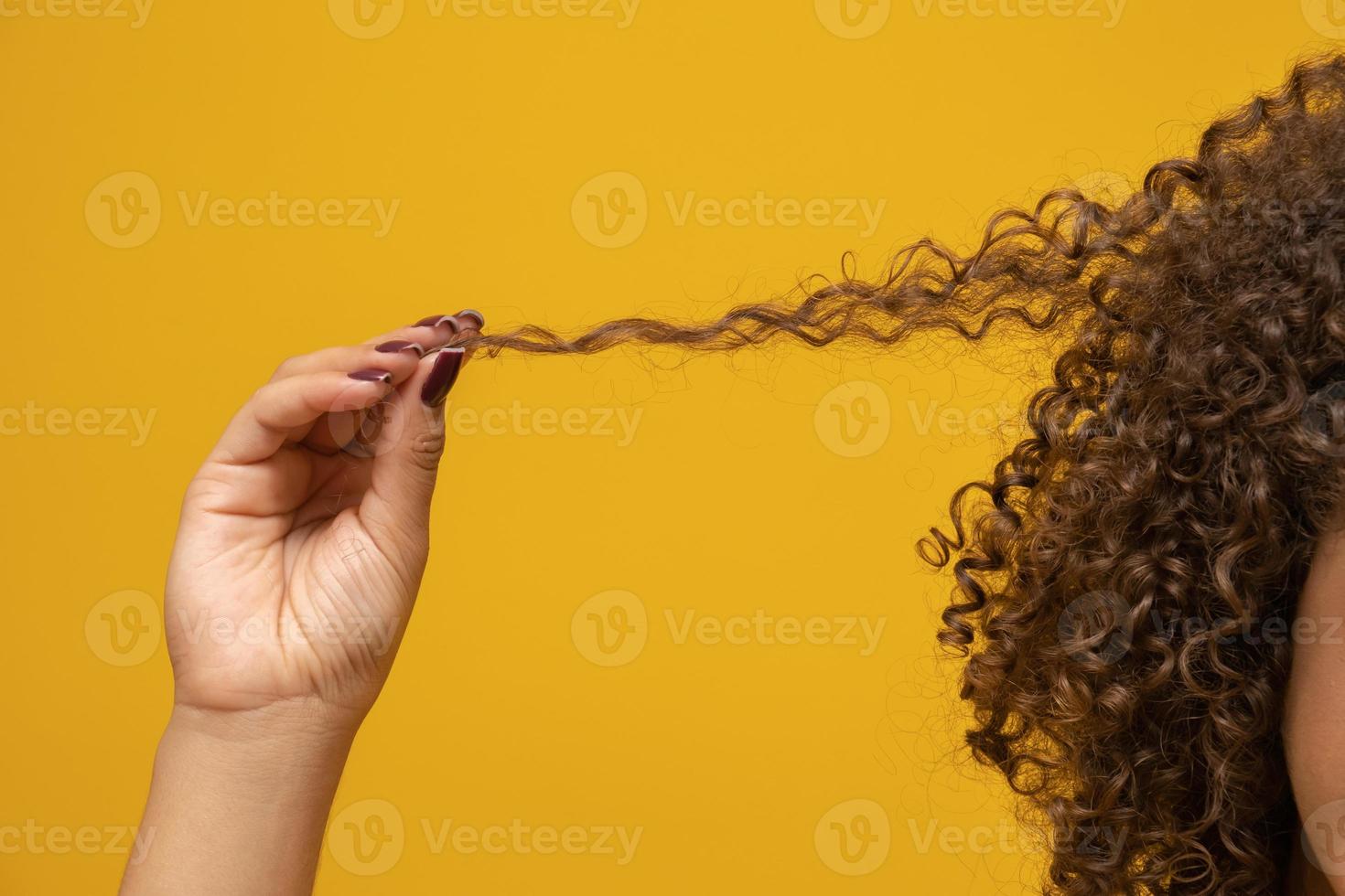 primer plano mujer africana americana tirando de un mechón de pelo. pelo rizado sobre fondo amarillo. foto