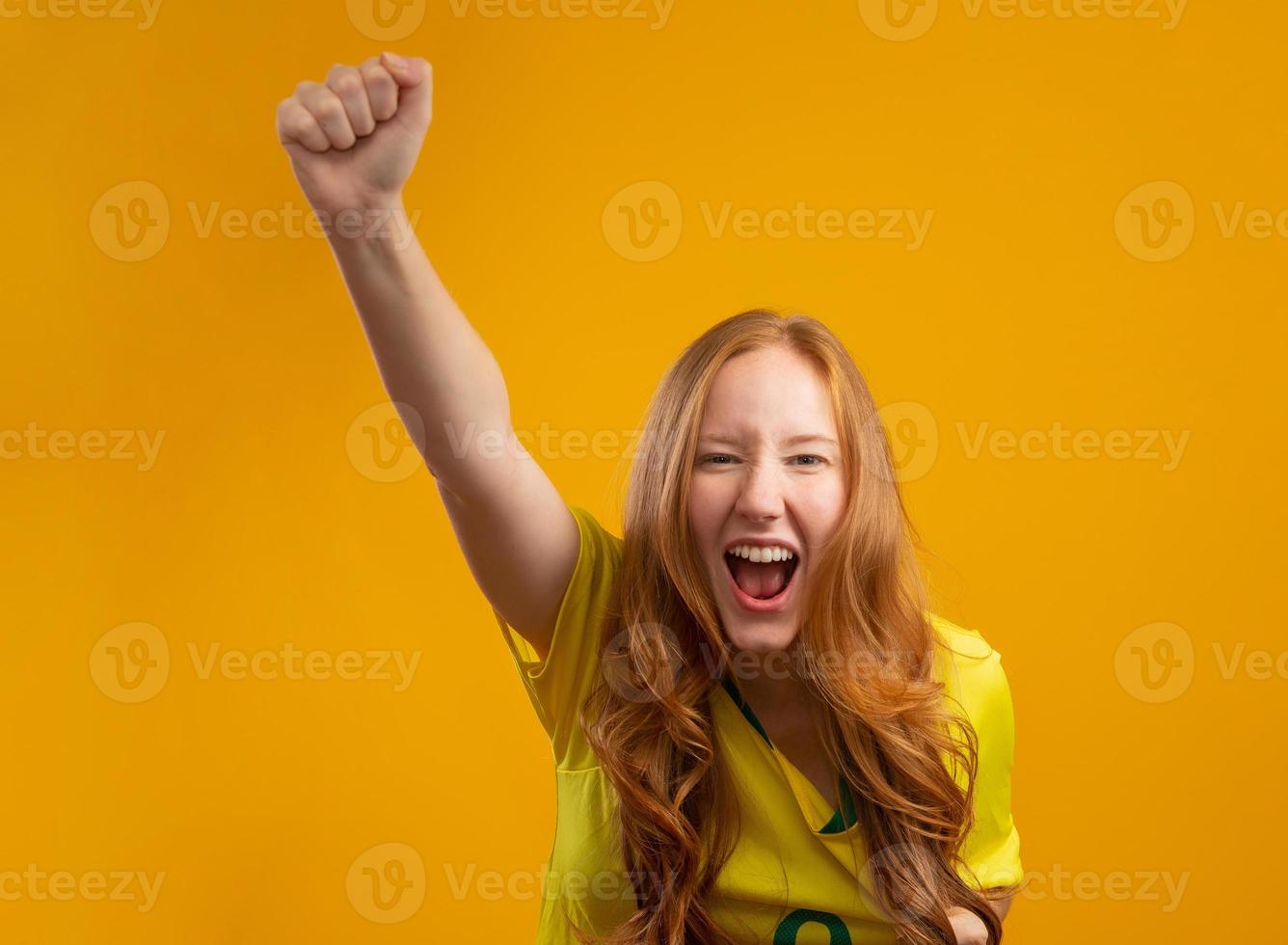 partidario de brasil. hincha brasileña pelirroja celebrando el fútbol, partido de fútbol con fondo amarillo. colores de brasil. foto