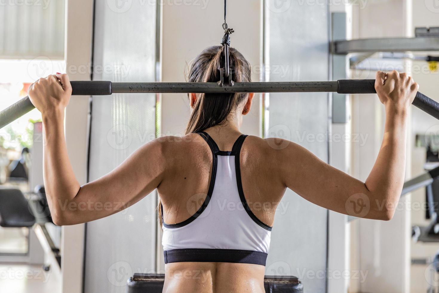 Athletic woman using machine for pumping back muscles in gym, back view photo