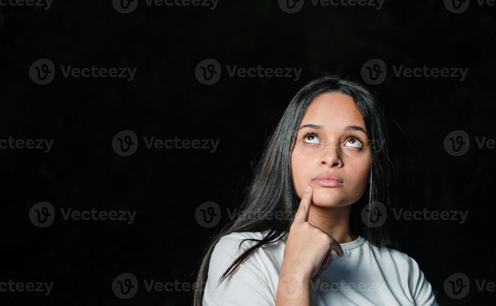 joven estudiante adolescente hermosa chica soñando pensando mirando de lado sobre fondo oscuro. foto