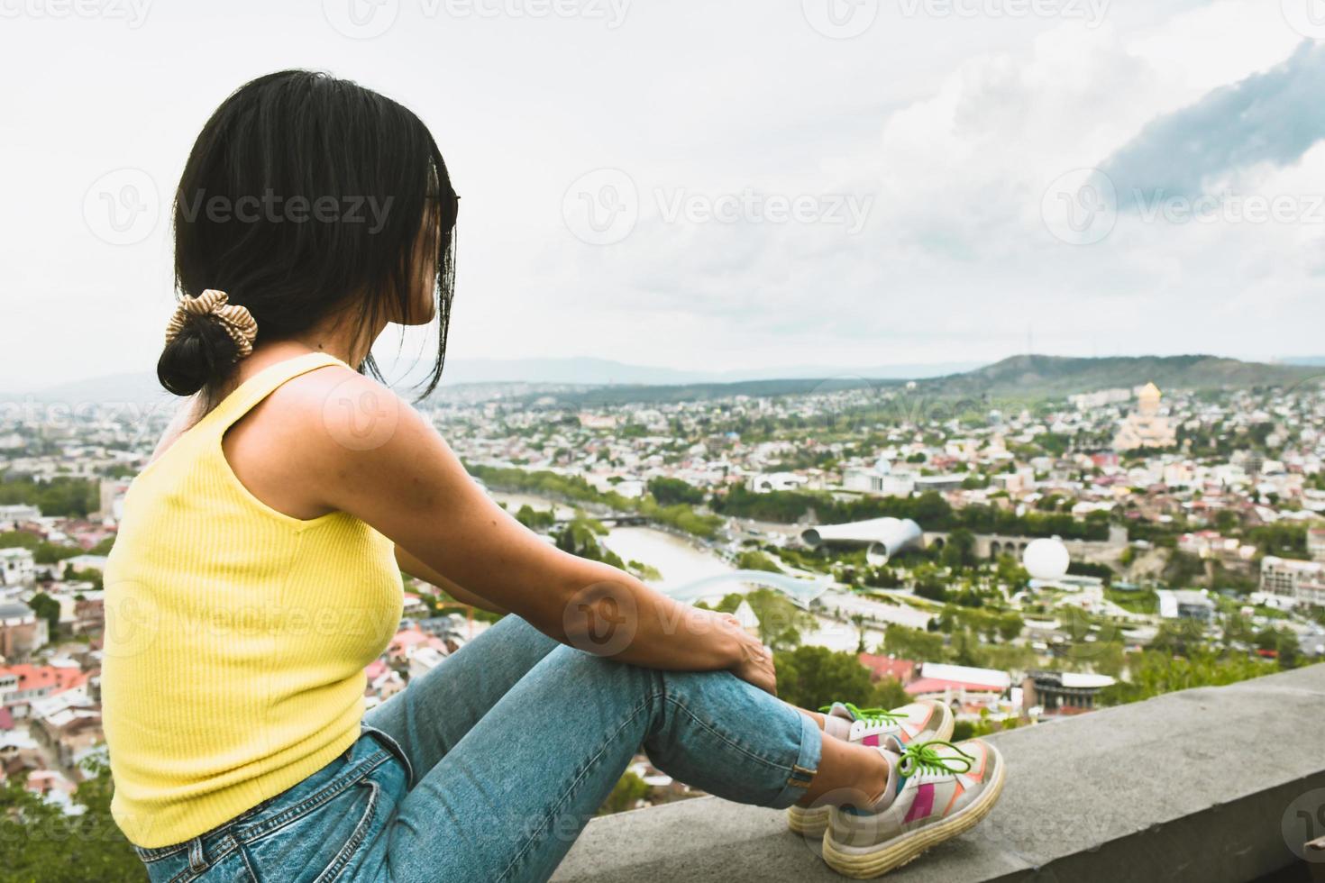 Attractive thoughtful female person sit on Narikala castle wall an enjoy view of Tbilisi city. Georgia travel destination photo