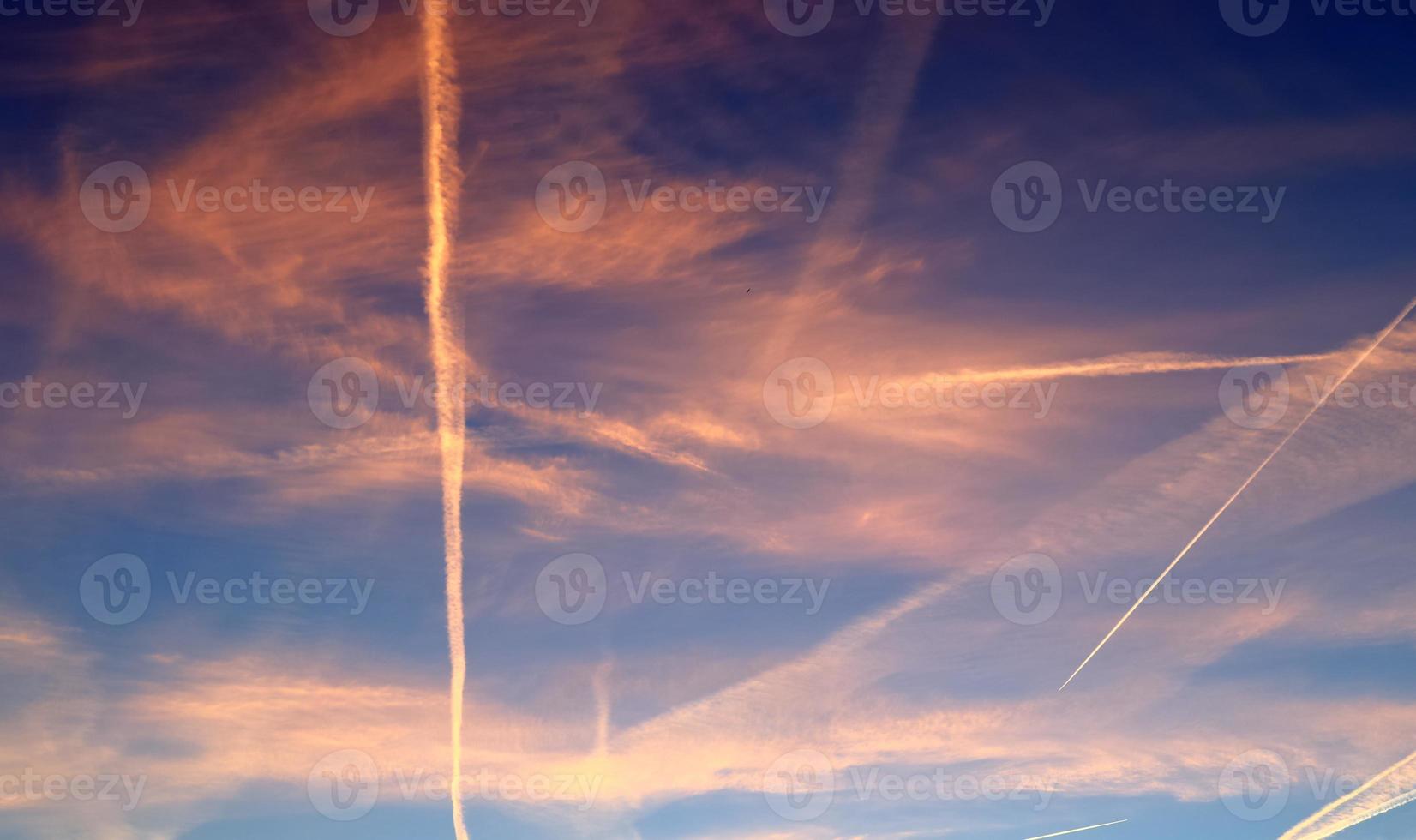 Aircraft condensation contrails in the blue sky inbetween some clouds photo