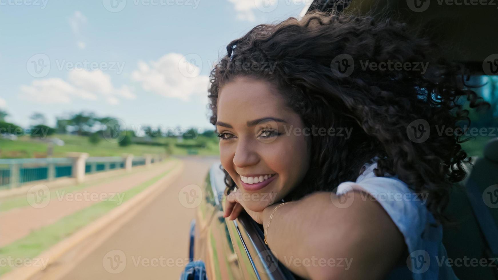 Latin woman in car window. Car trip. Curly hair in wind. Girl looks out of car window. photo