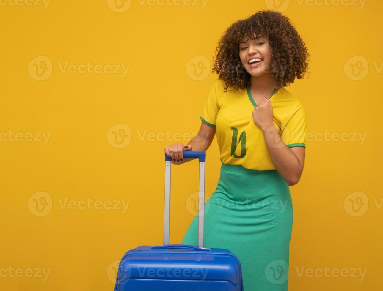 Funny woman holding a heavy travel bag. On yellow background. Brazilian player with bags ready to see Brazil play in the World Cup photo