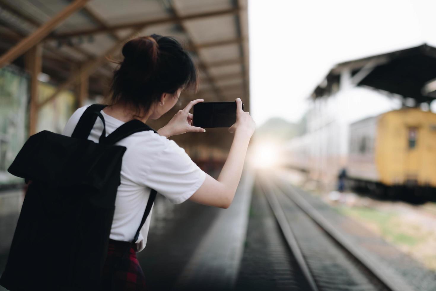 Tourist woman aling selfie with a smartphone while at the train station. Enjoying travel concept. Girl using smartphone while at the railway station platform. photo