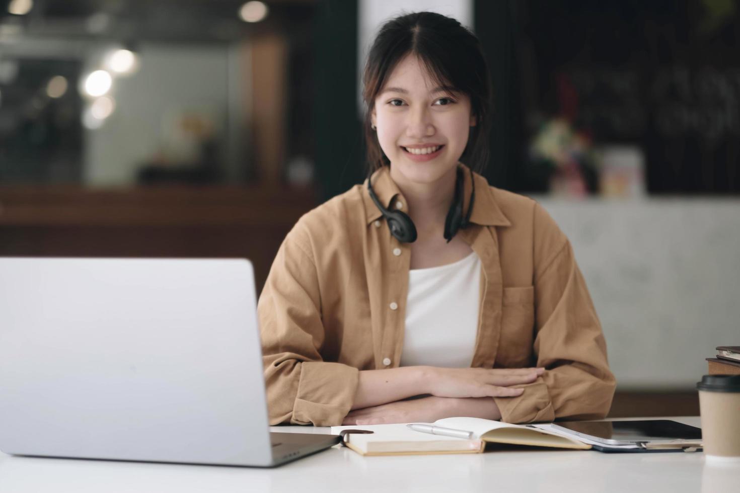 Happy young Asian student woman wearing headphones looking at webcam, looking at camera, during virtual meeting or video call talk. photo