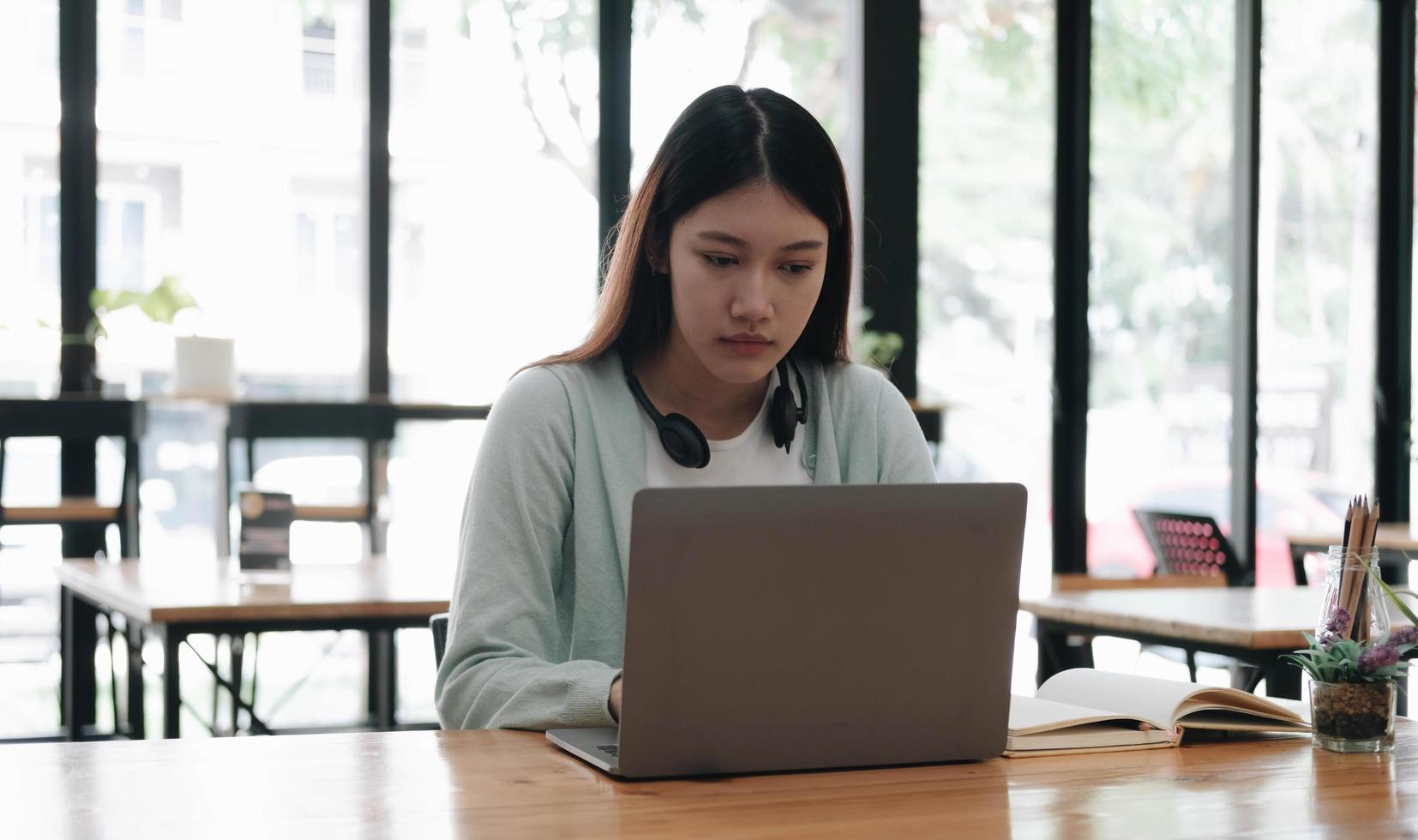 estudiante asiático serio y enfocado que usa una laptop en la cocina, mira la pantalla con atención y concentración, ve un seminario web de aprendizaje, capacitación virtual, curso de video, estudia desde casa foto