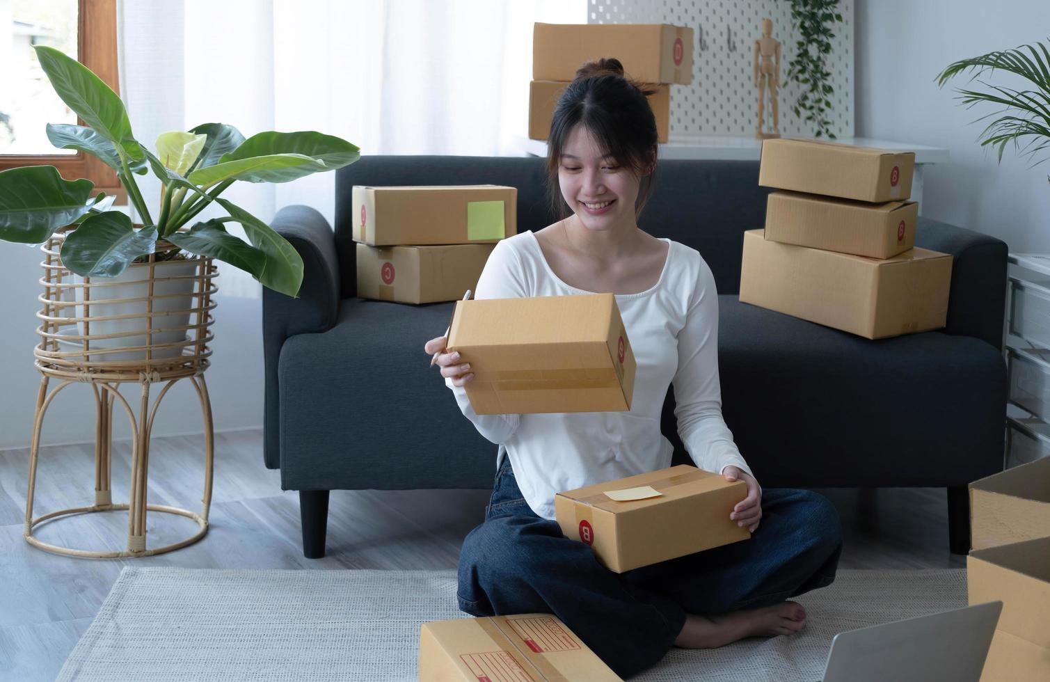 joven empresaria asiática, adolescente dueña de un negocio en línea que trabaja en casa, mujeres empacando el producto que el cliente ordena desde el sitio web, entregado como un paquete, utiliza los servicios de la empresa de envío de paquetes foto