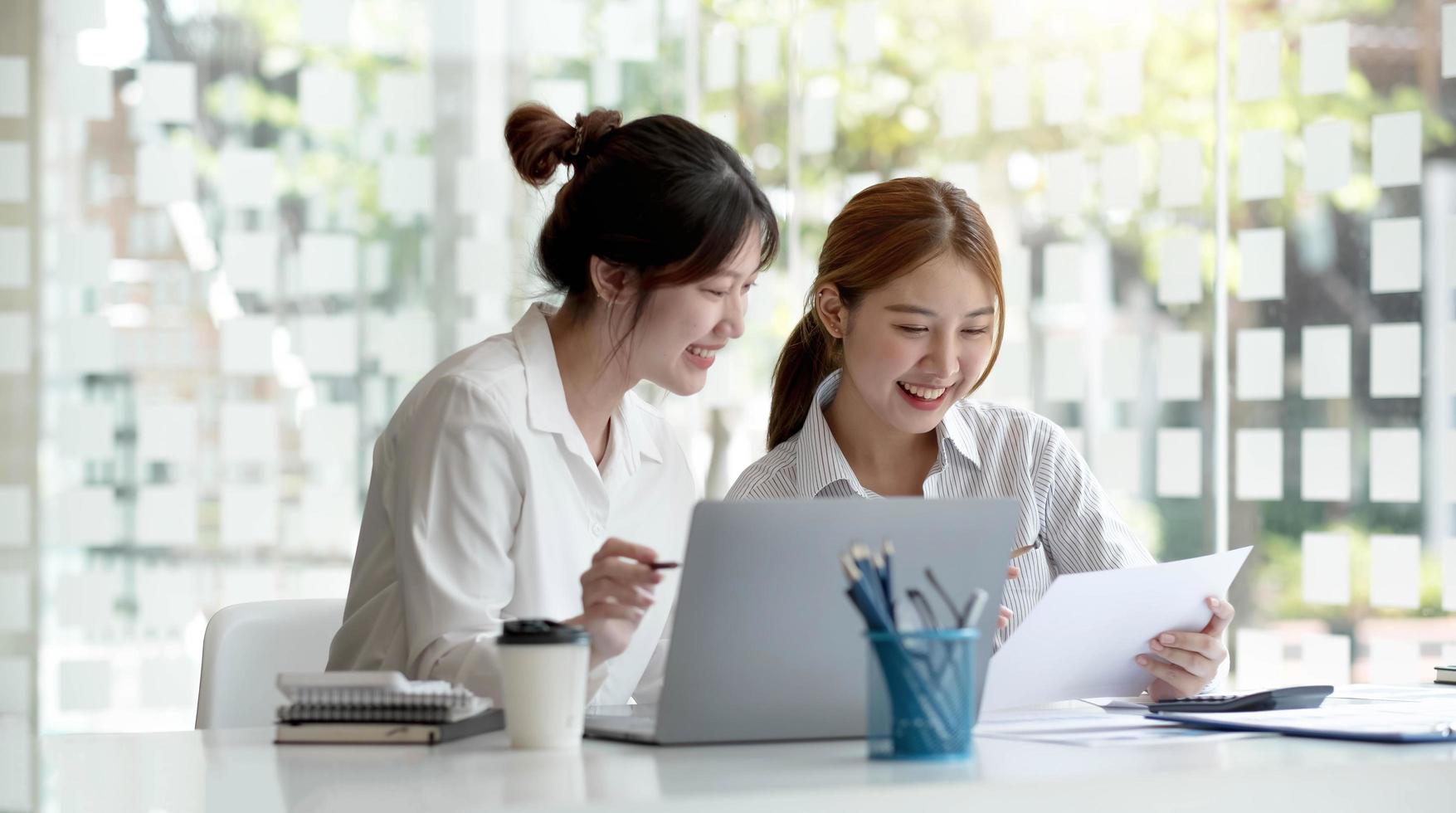 Two young Asian businesswoman discuss investment project working and planning strategy. Business people talking together with laptop computer at office. photo