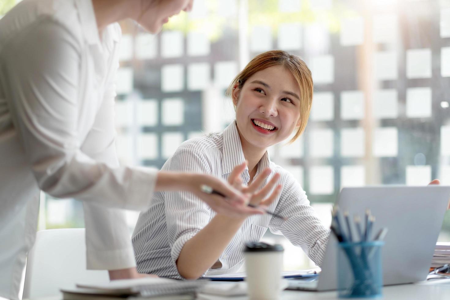 dos jóvenes empresarias trabajadoras que trabajan juntas en sus computadoras portátiles leen pantallas con caras sonrientes en ángulos altos. foto