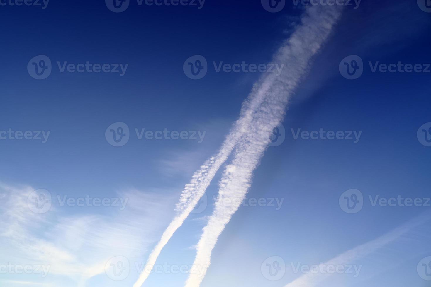 Aircraft condensation contrails in the blue sky inbetween some clouds photo