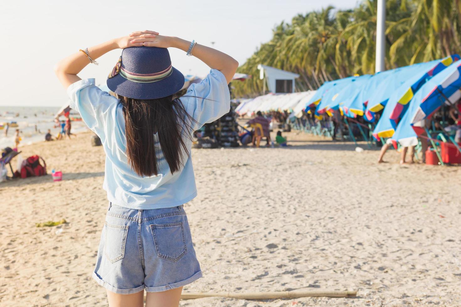 la chica con una camisa azul y jeans cortos con un sombrero azul está parada de espaldas en la playa. foto