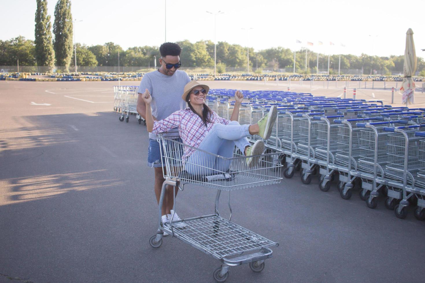 Happy young couple riding on trolley on empty mall parking , hipster friend have good time during shopping, couple in love riding on shopping cart photo