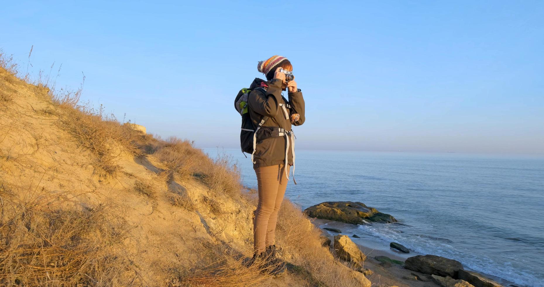 joven viajera con mochila y cámara de cine retro viaja en las montañas de otoño cerca del mar foto