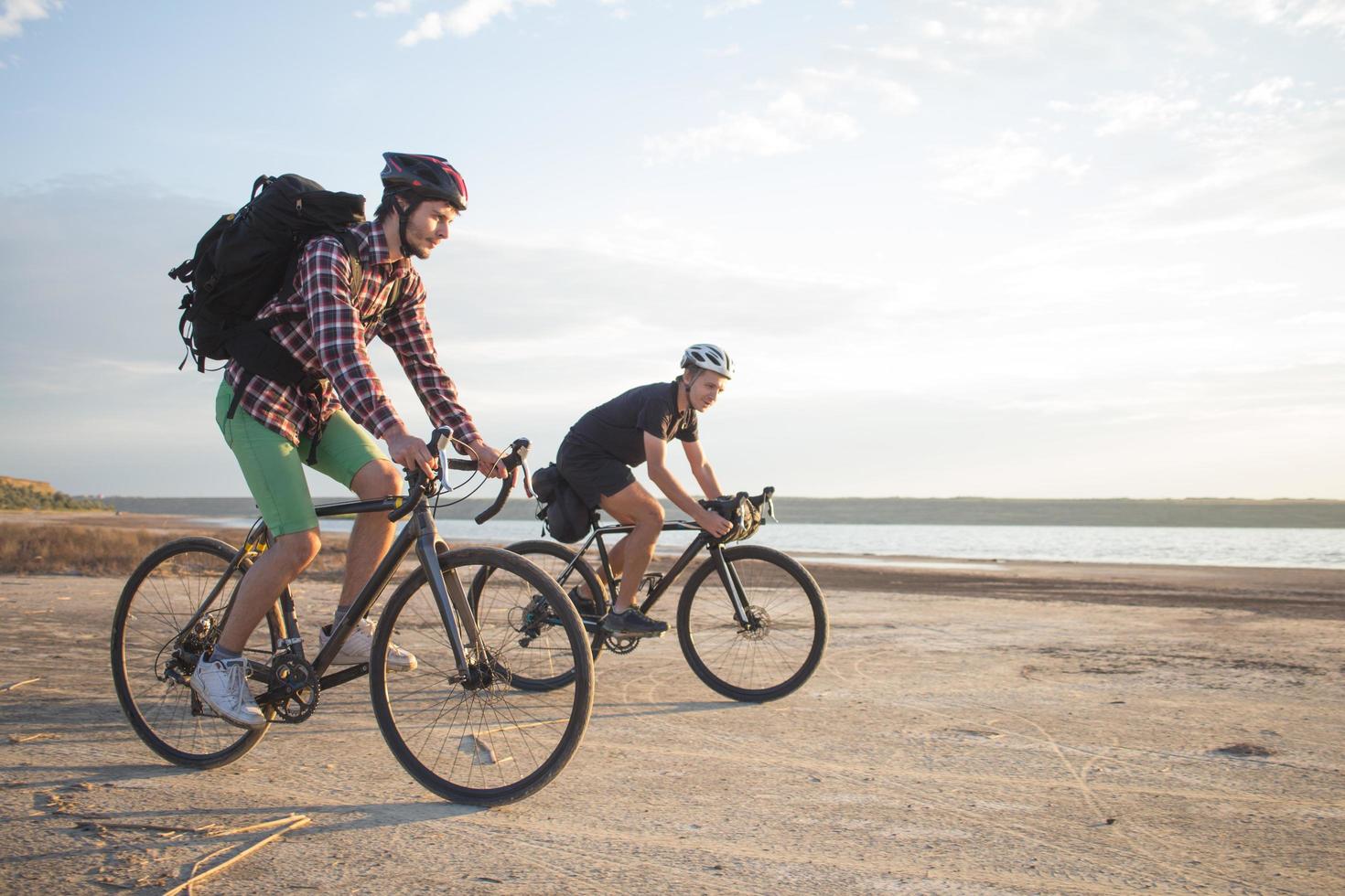 dos jóvenes en una bicicleta de gira con mochilas y cascos en el desierto en un viaje en bicicleta foto