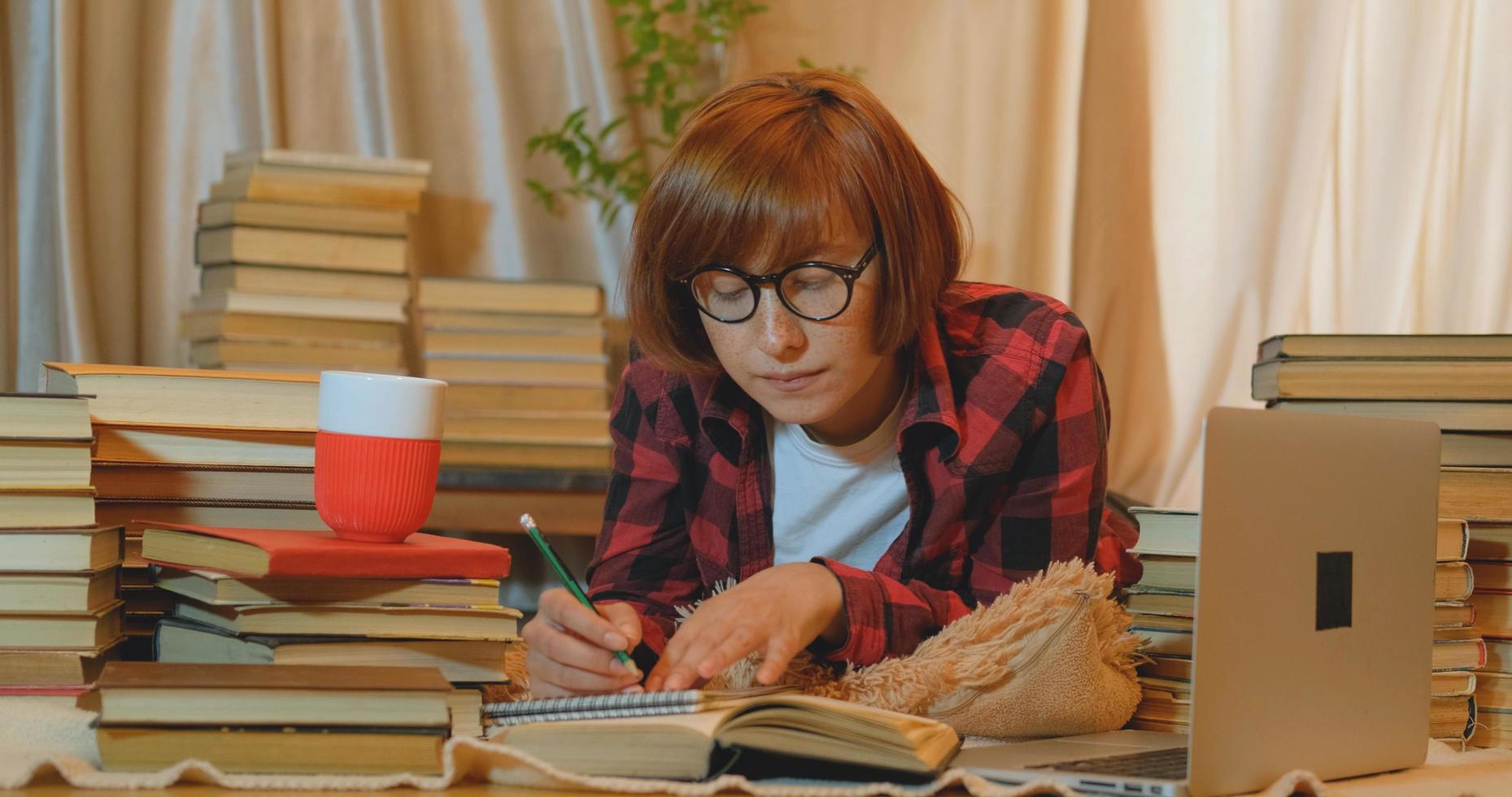 Young woman student studying at home with many books and laptop photo