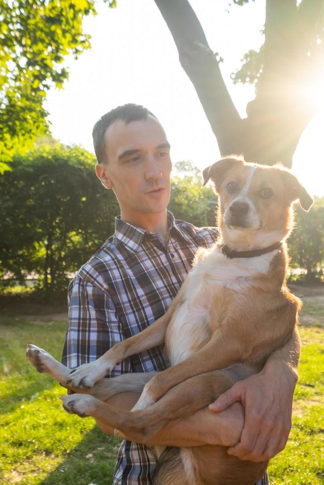 un joven feliz juega con un perro que no es de raza en el parque soleado de verano foto