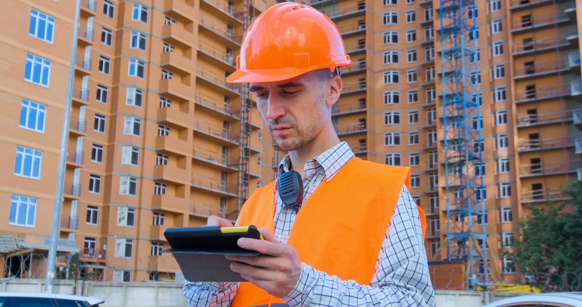 retrato de un especialista en construcción con casco naranja y chaleco de seguridad contra un gran edificio foto