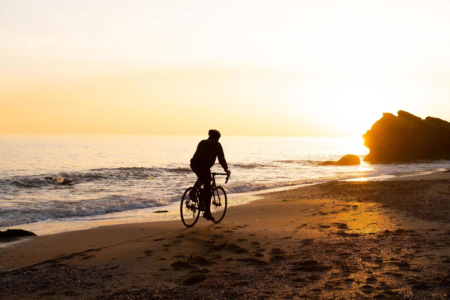 silhouette of young male bicycle rider in helmet on the beach during beautiful sunset photo