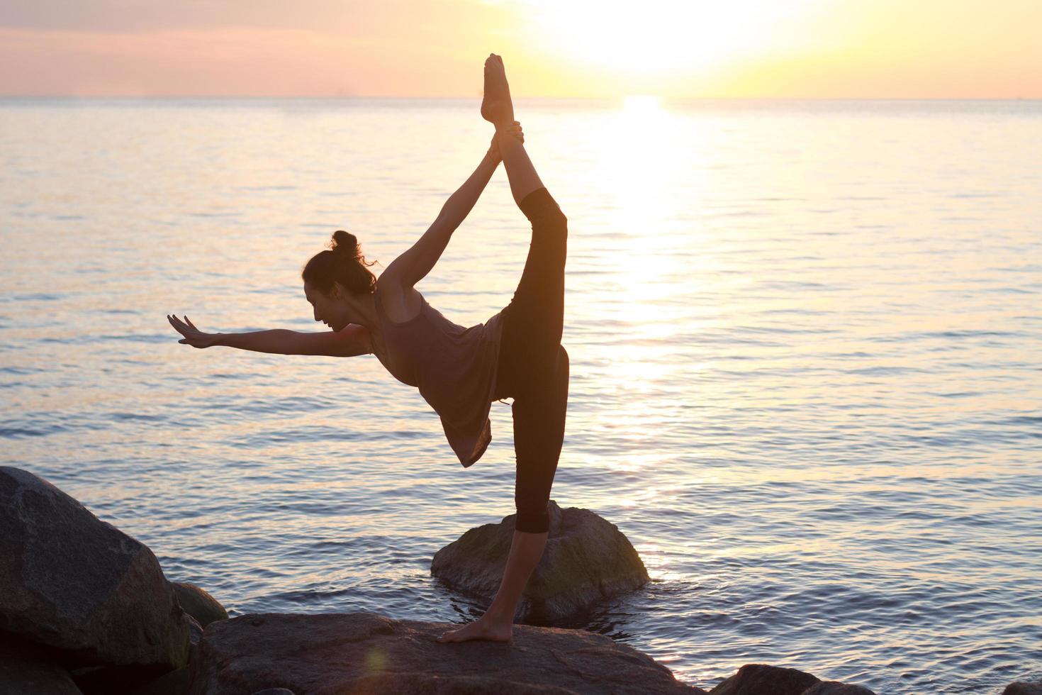 Fitness mujer asiática de raza mixta en pose de yoga en la playa de la mañana, hermosa mujer en forma practica fitness exrxise piedras, mar de la mañana o fondo del océano foto