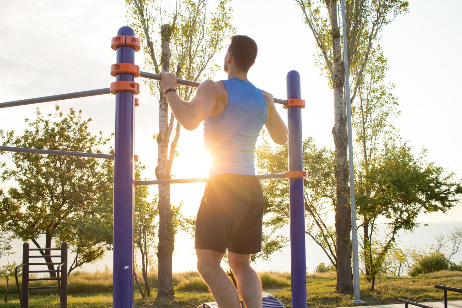 hombre musculoso haciendo pull-ups en la barra horizontal, entrenamiento de hombre fuerte en el gimnasio del parque al aire libre por la mañana. foto