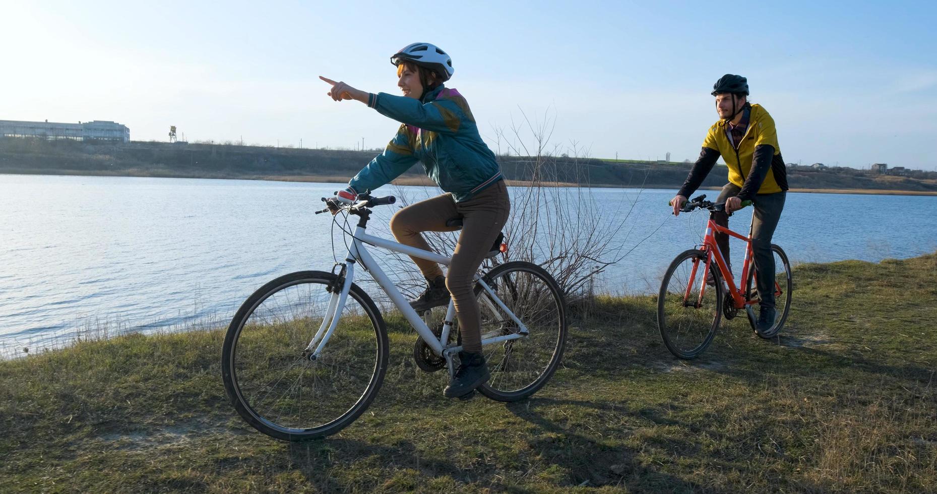 Couple of male and female ride on bicycles near river during sunset photo