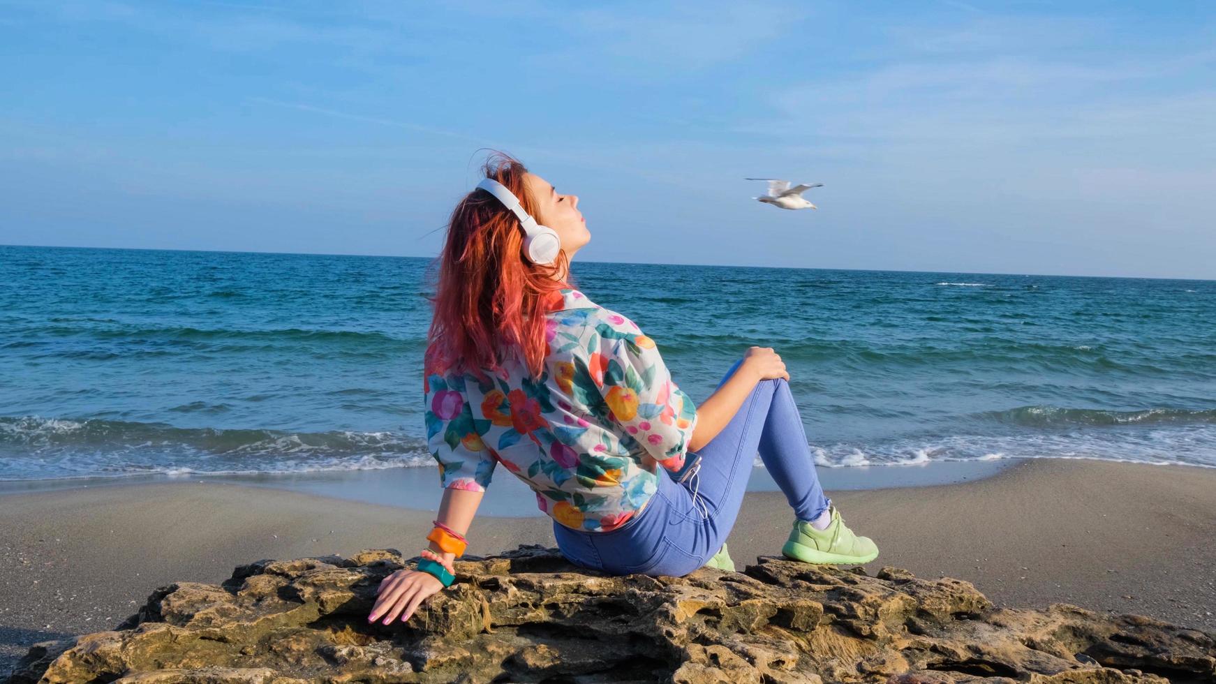 mujer joven con cabello colorido camina en la playa de verano y escucha música con auriculares foto