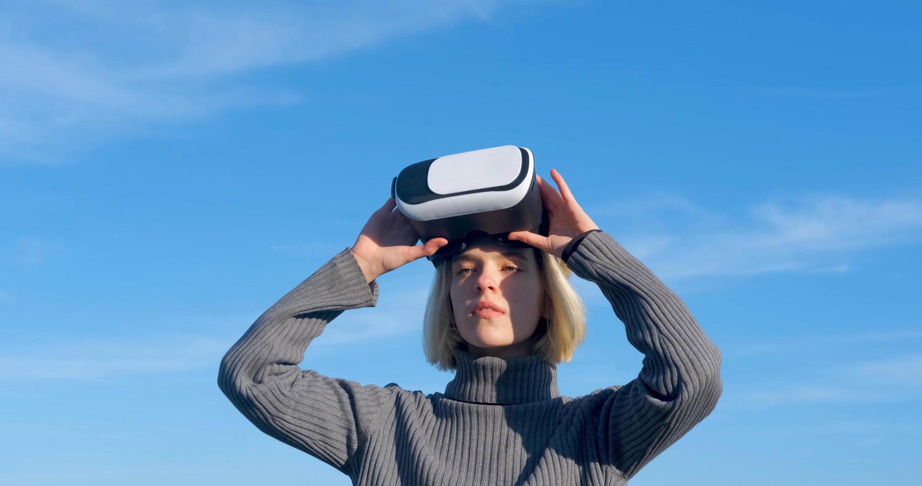 mujer joven y guapa con gafas de realidad virtual al aire libre en la playa contra el cielo azul soleado foto