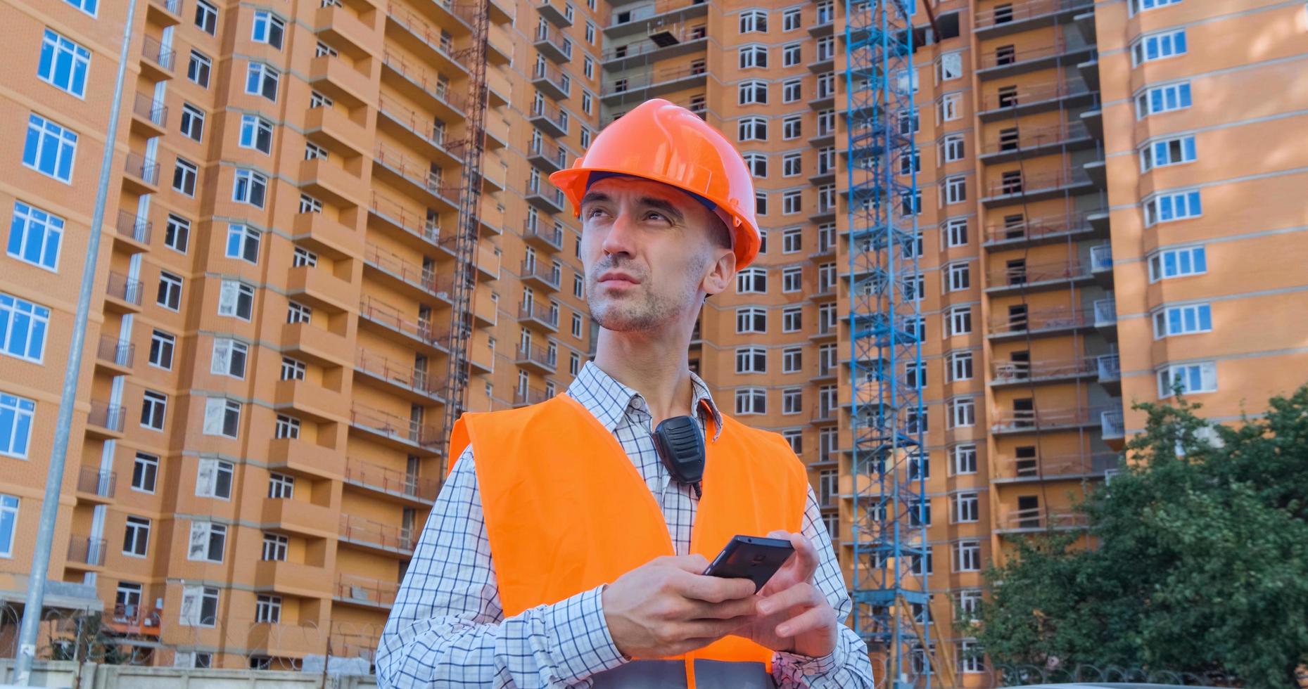 retrato de un especialista en construcción con casco naranja y chaleco de seguridad contra un gran edificio foto