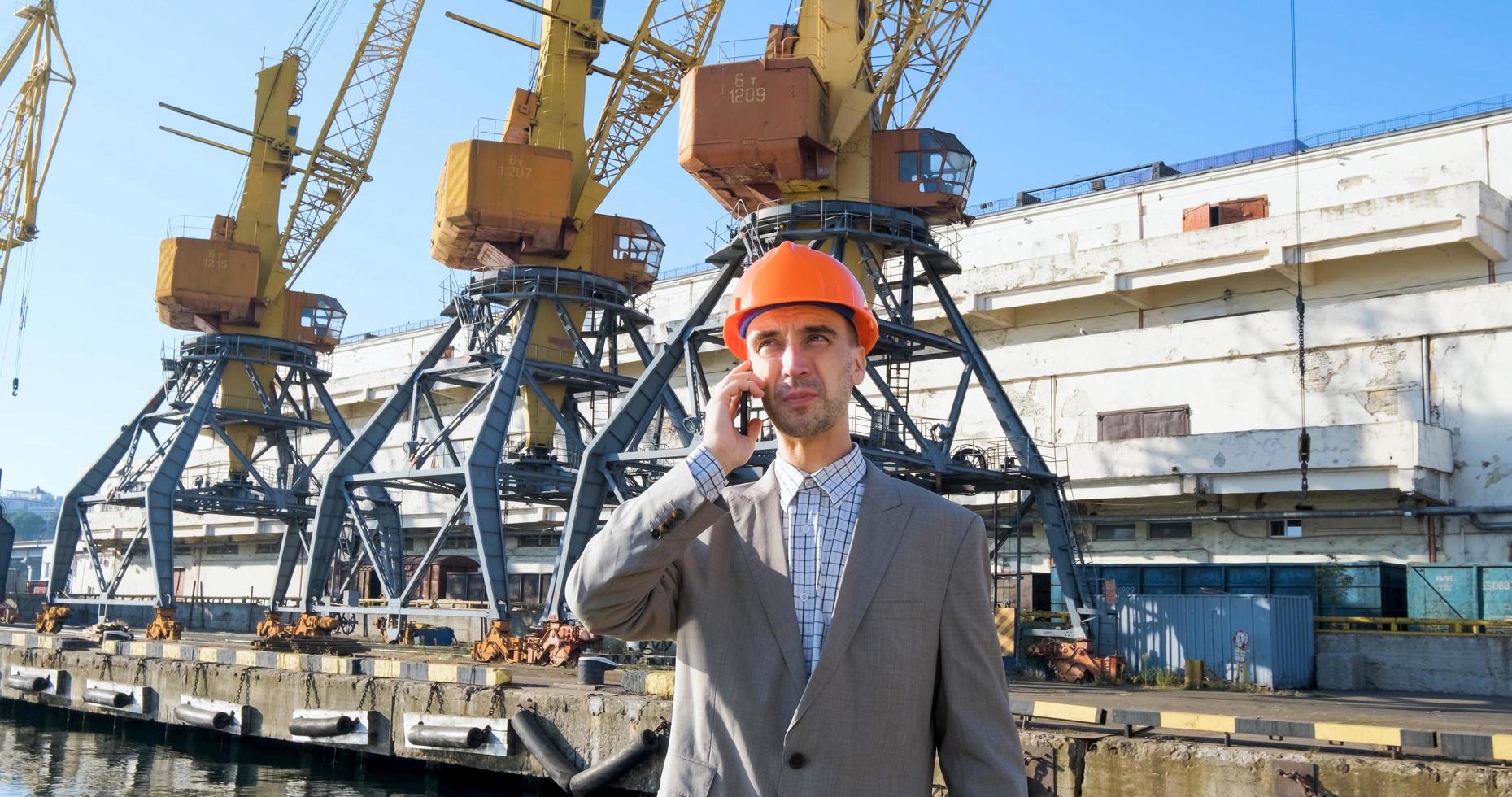 Young male worker of sea harbor in helmet, cargo manager in suit and halmet works outdoor , cranes and sea background photo