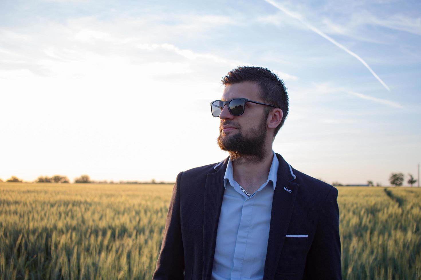 retrato de un joven con traje y gafas de sol, fondo de campos de trigo de verano foto