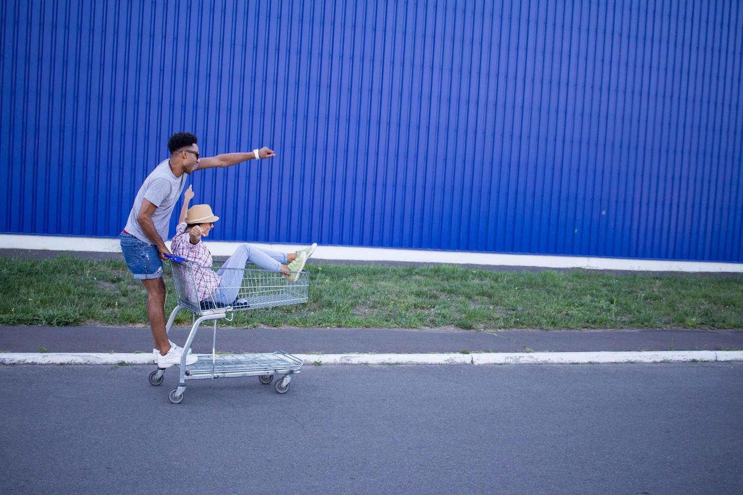 feliz pareja joven montando en tranvía en un estacionamiento vacío del centro comercial, un amigo hipster se lo pasa bien durante las compras, una pareja enamorada montando en un carrito de compras foto