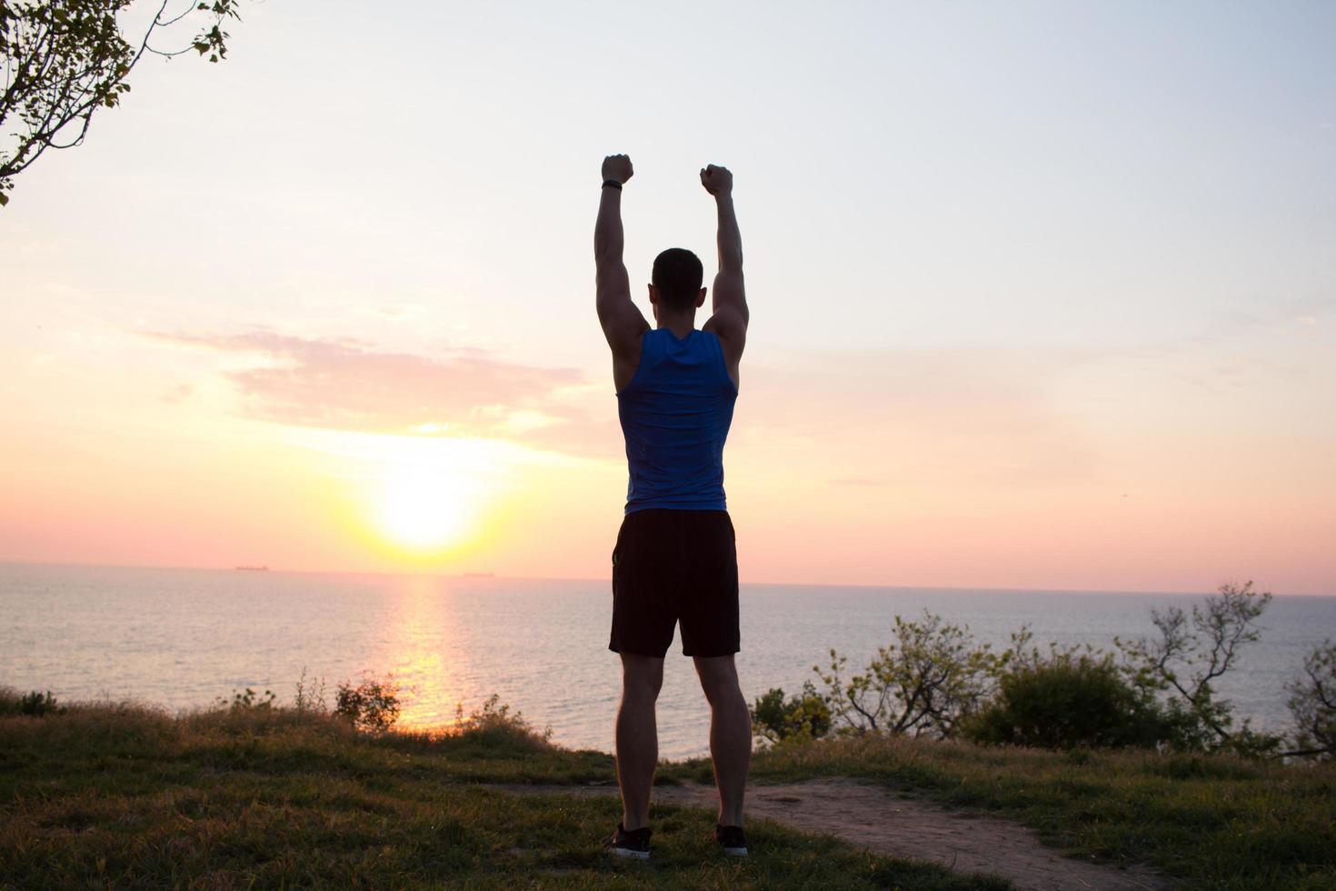 ajuste el entrenamiento de corredores masculinos en la playa de verano y escuche música contra el hermoso cielo y el mar foto