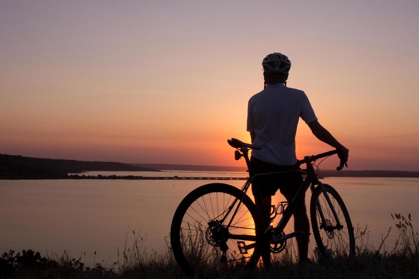 silhouette of a cyclist watching sunset in lake, male bicycle rider in helmet during sunset photo