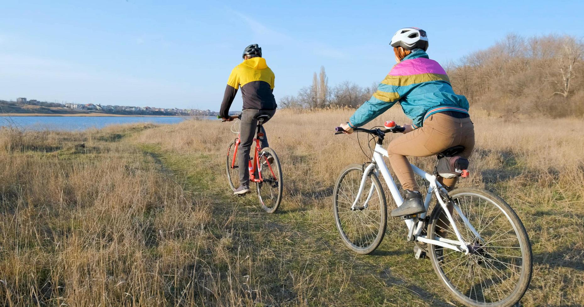 Couple of male and female ride on bicycles near river during sunset photo