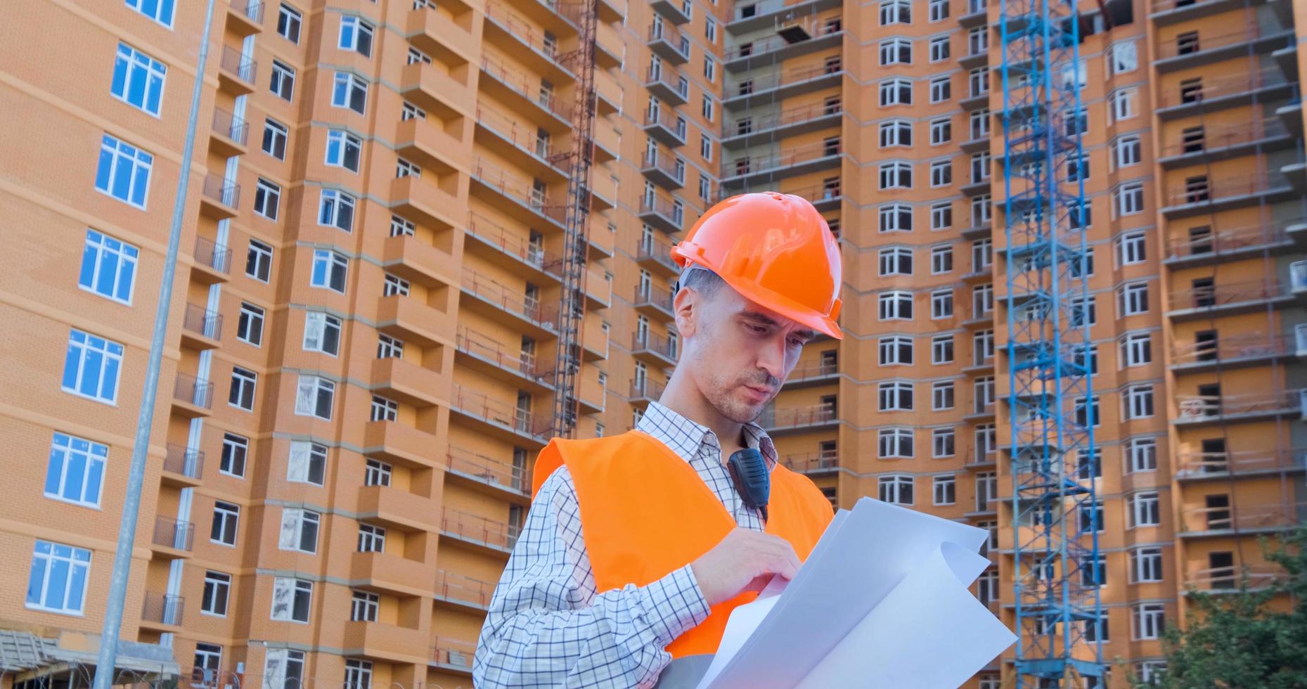 retrato de un especialista en construcción con casco naranja y chaleco de seguridad contra un gran edificio foto