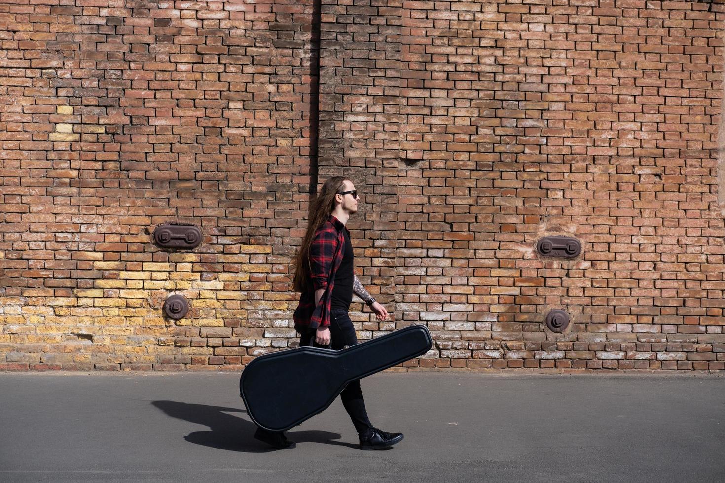 Young male with long hair and tattoo play on acoustic guitar outdoors on the street photo